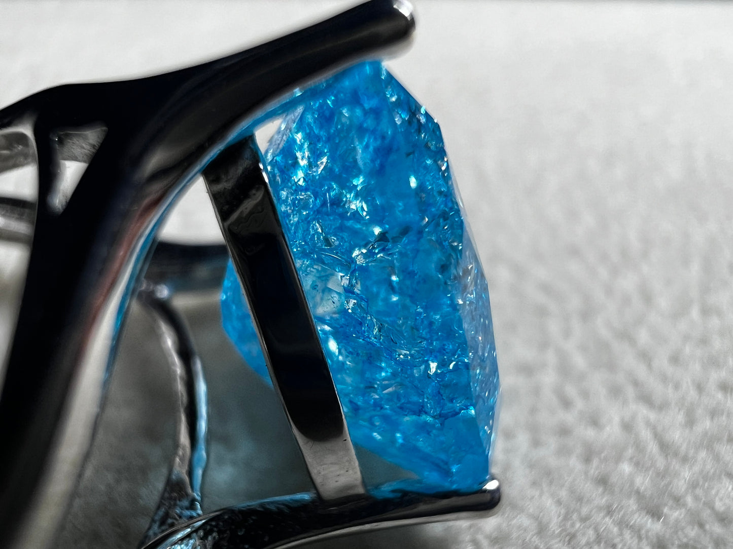 This sterling silver ring showcases a large, blue trilliant cut crackled quartz, creating a captivating centerpiece. Perfect for adding a touch of elegance and distinctiveness to any outfit.