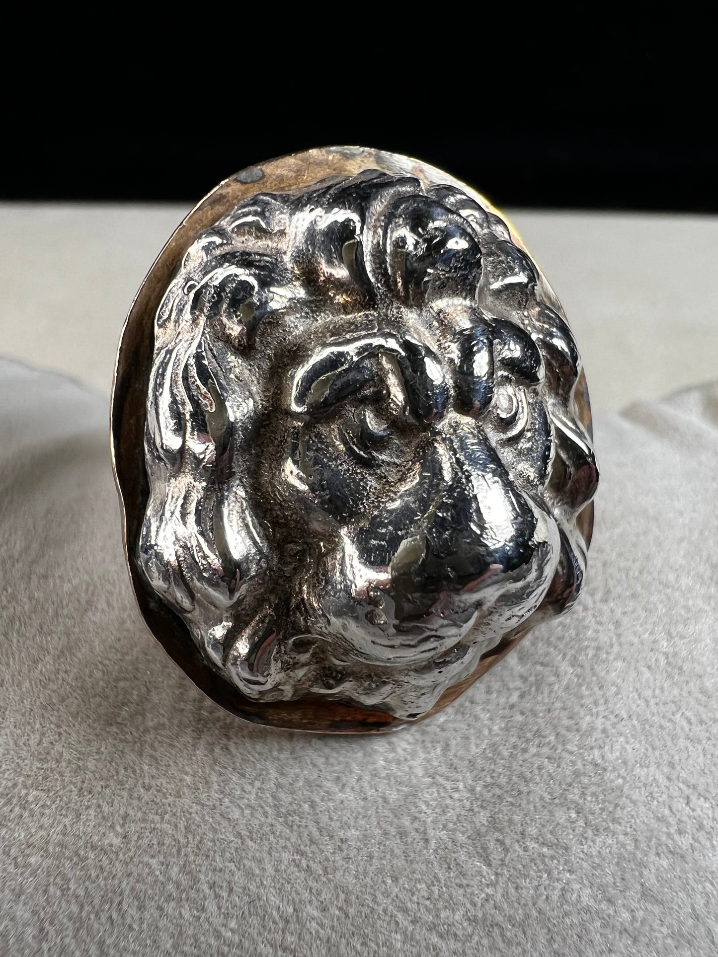 This sterling silver ring by Loving Anvil features a striking lion's head design, expertly crafted for a bold and unique statement. The backing plate is finished in fine gold, adding a stylish two-tone effect.