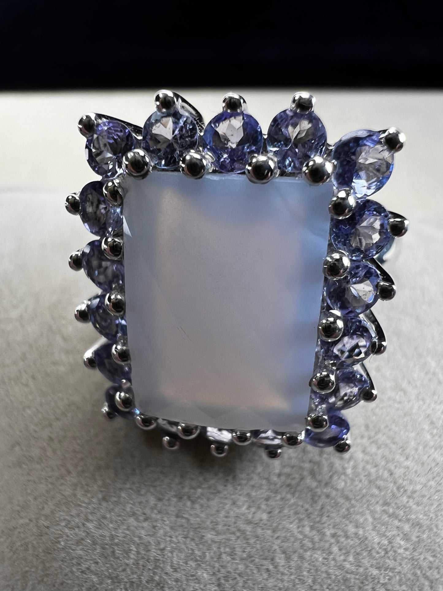 This sterling silver ring combines comfortable wear with captivating style. Featuring a large chalcedony centerpiece surrounded by sparkling tanzanite accent stones, this piece offers a stunning and elegant look.
