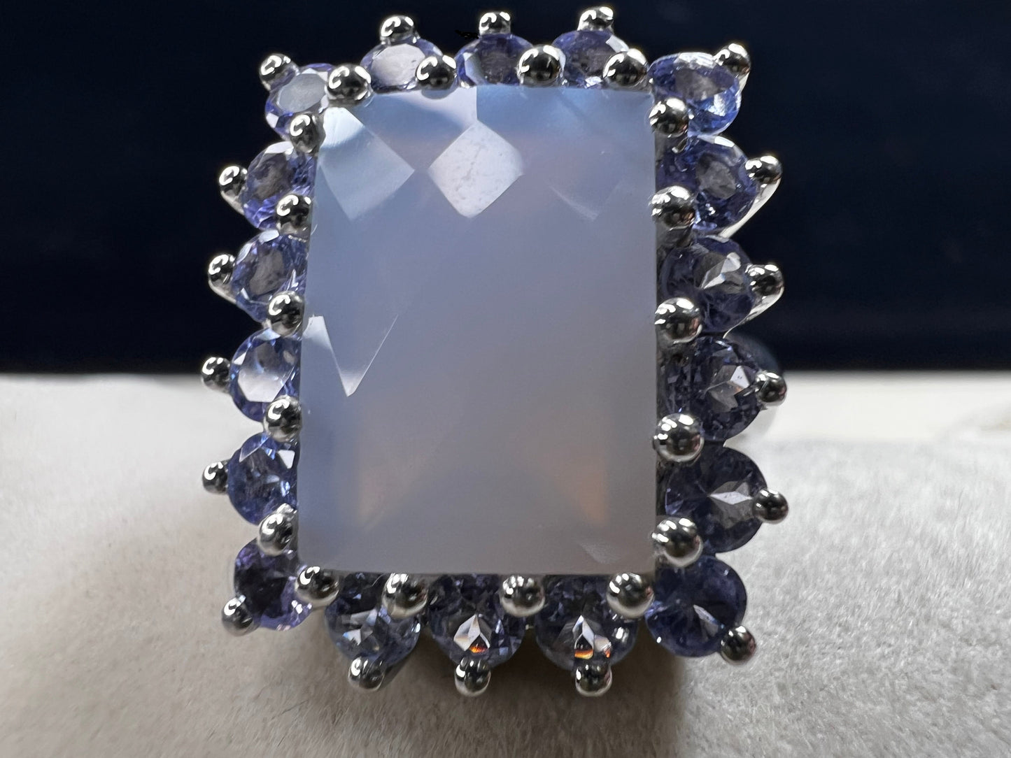 This sterling silver ring combines comfortable wear with captivating style. Featuring a large chalcedony centerpiece surrounded by sparkling tanzanite accent stones, this piece offers a stunning and elegant look.