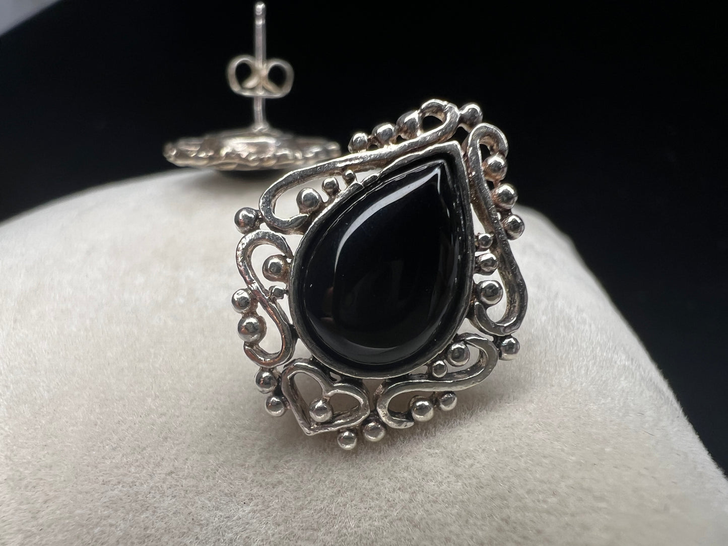 These earrings showcase teardrop-shaped onyx stones with intricate silver work surrounding them. The unique silver work design features a small heart at the bottom of each earring.