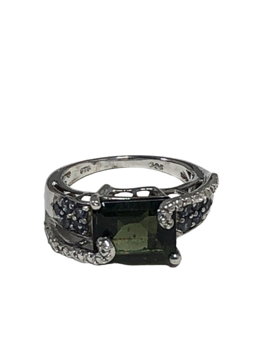 This ring oozes elegance and individuality. Crafted with fine sterling silver, it features a faceted glass stone with a green hue. The stones on each side of the centerpiece add subtle flashes of blue.
