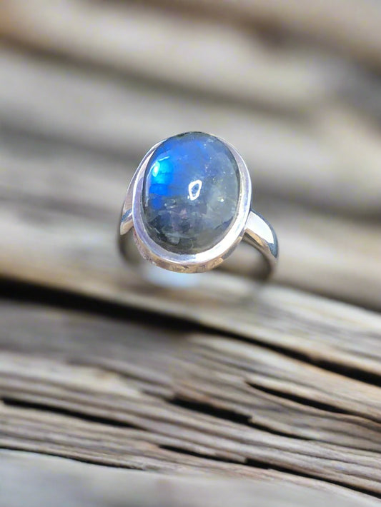 This sterling silver ring features a domed labradorite cabochon, also known in the trade as rainbow moonstone, with a greenish-gray body that flashes brilliant blue in the light. Its sleek bezel setting highlights the stone’s natural play of color, making it a captivating piece.