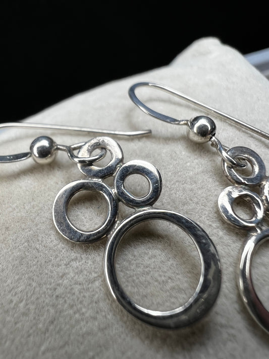 These elegant sterling silver dangle earrings feature an eye-catching arrangement of circles in varying sizes, creating a playful yet minimalist look.