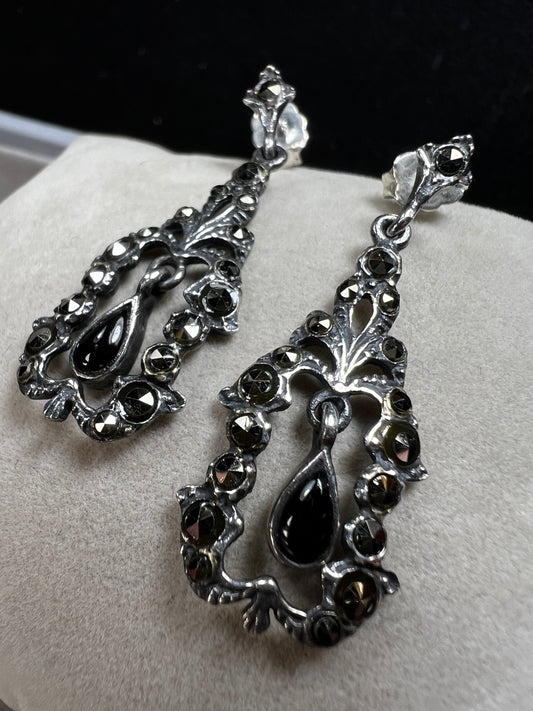 These sterling silver earrings shimmer with marcasite accents and showcase a dangling teardrop of onyx, adding timeless charm and subtle movement.