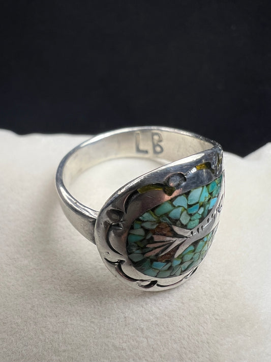 This expertly crafted vintage sterling silver ring, signed LB, showcases intricate detailing that captures timeless elegance. Accented with turquoise chips, it offers a distinctive and striking look, perfect for collectors or anyone seeking a unique piece with authentic vintage charm.