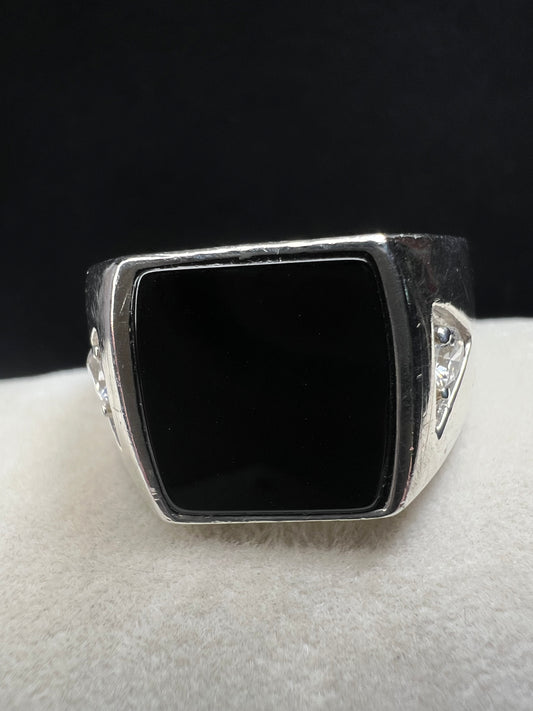 This vintage Avon ring showcases a prominent onyx cabochon flanked by two small cubic zirconias. Designed in a larger size, it is suitable for both men and women.