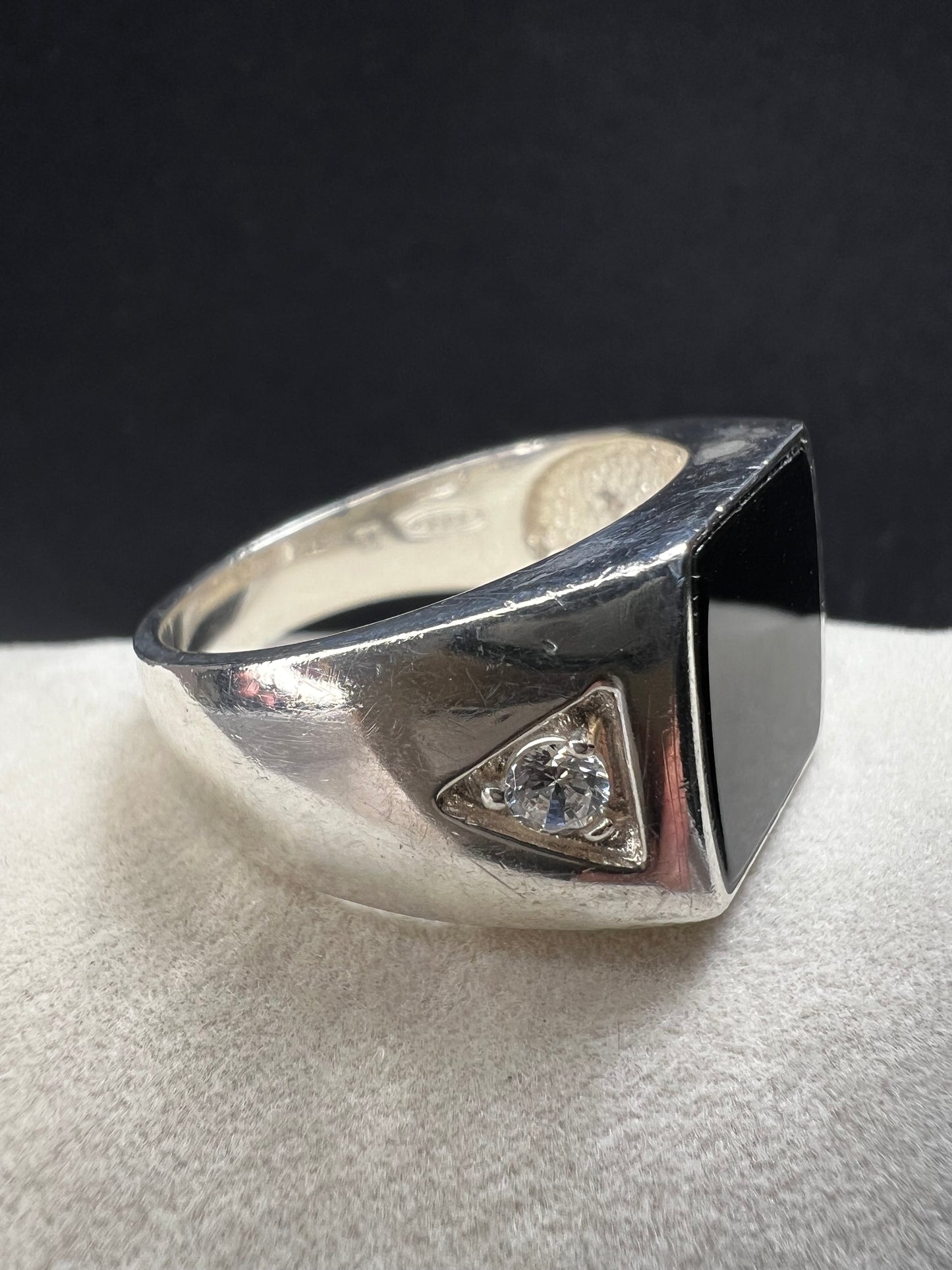 This vintage Avon ring showcases a prominent onyx cabochon flanked by two small cubic zirconias. Designed in a larger size, it is suitable for both men and women.