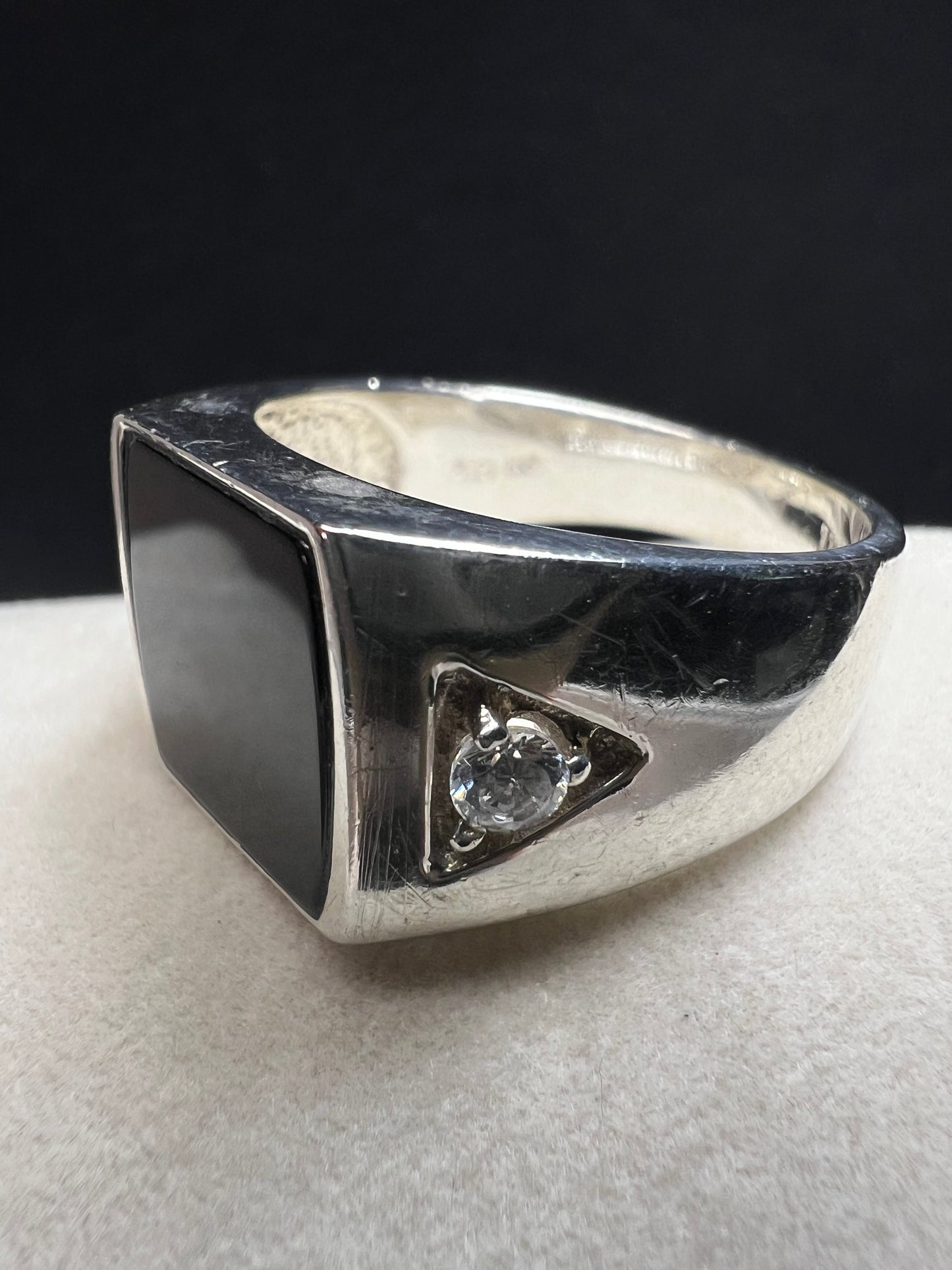 This vintage Avon ring showcases a prominent onyx cabochon flanked by two small cubic zirconias. Designed in a larger size, it is suitable for both men and women.