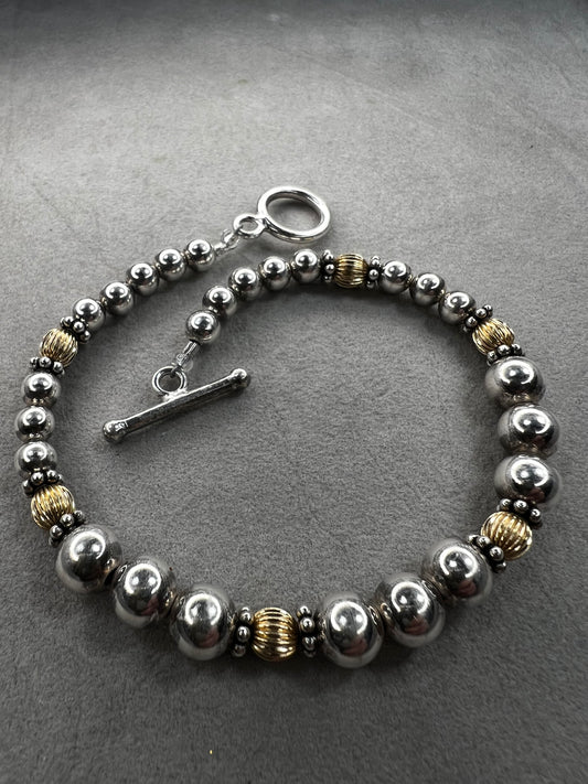 This sterling silver bracelet showcases a refined design with graduated beads, six of which are accented by a gold overlay. The contrasting two-tone finish adds depth and elegance, making it a versatile accessory for both casual and formal wear.