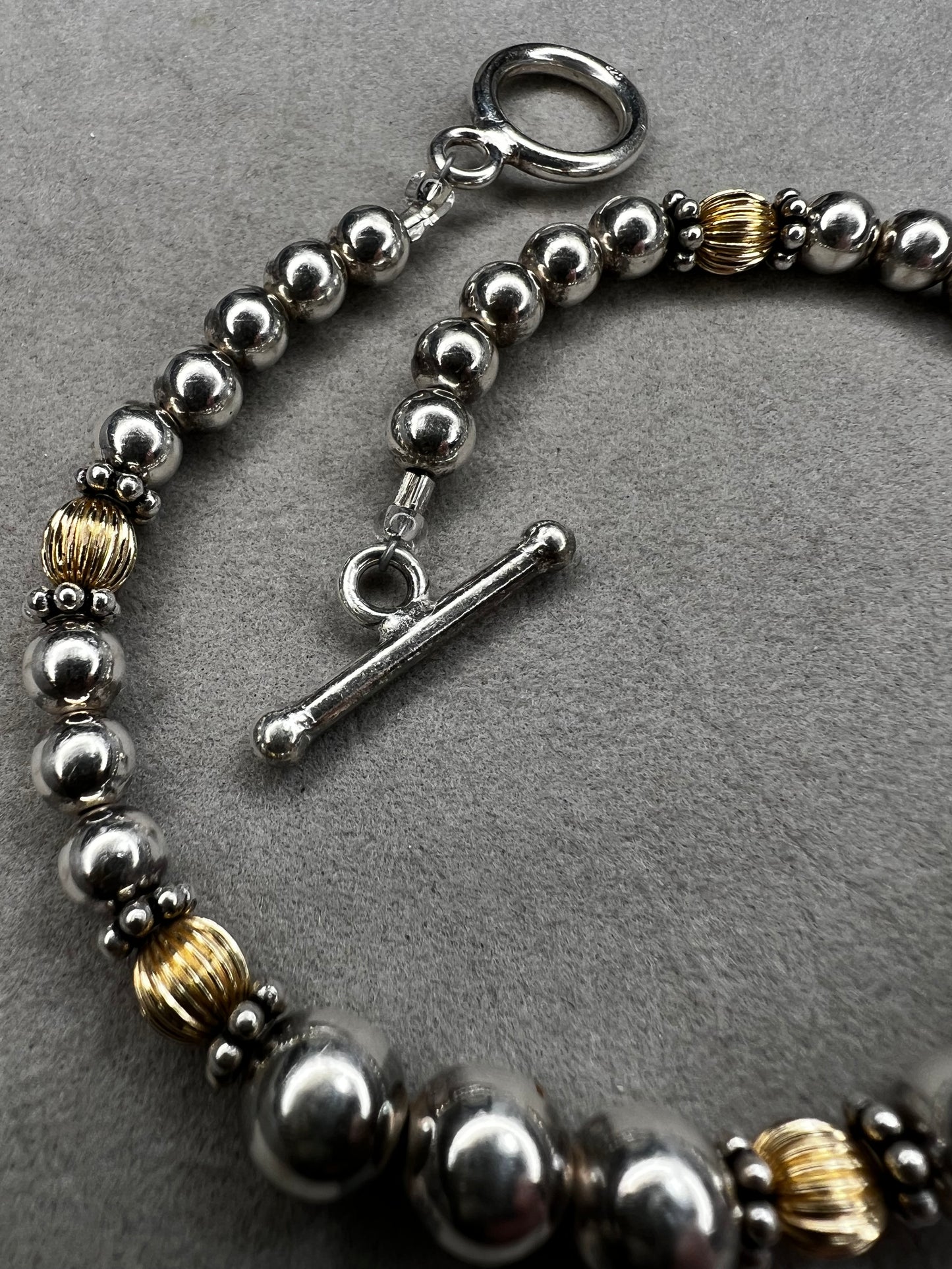 This sterling silver bracelet showcases a refined design with graduated beads, six of which are accented by a gold overlay. The contrasting two-tone finish adds depth and elegance, making it a versatile accessory for both casual and formal wear.