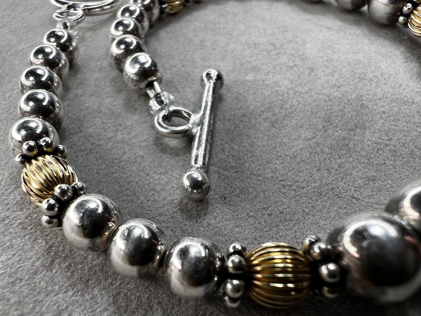 This sterling silver bracelet showcases a refined design with graduated beads, six of which are accented by a gold overlay. The contrasting two-tone finish adds depth and elegance, making it a versatile accessory for both casual and formal wear.