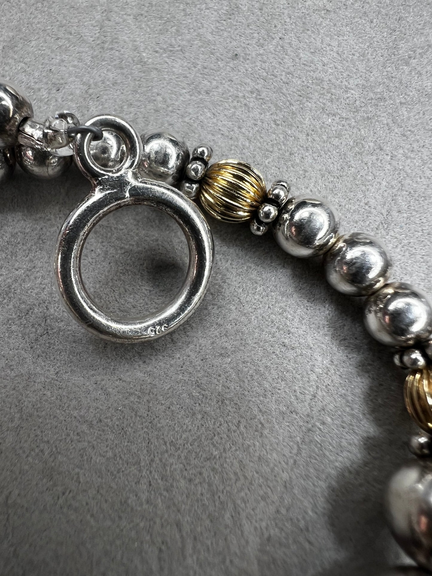 This sterling silver bracelet showcases a refined design with graduated beads, six of which are accented by a gold overlay. The contrasting two-tone finish adds depth and elegance, making it a versatile accessory for both casual and formal wear.