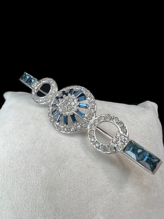 This exquisite sterling silver brooch showcases a refined arrangement of blue and white rhinestones, embodying the elegance of Hollywood Regency design. Signed Otis.