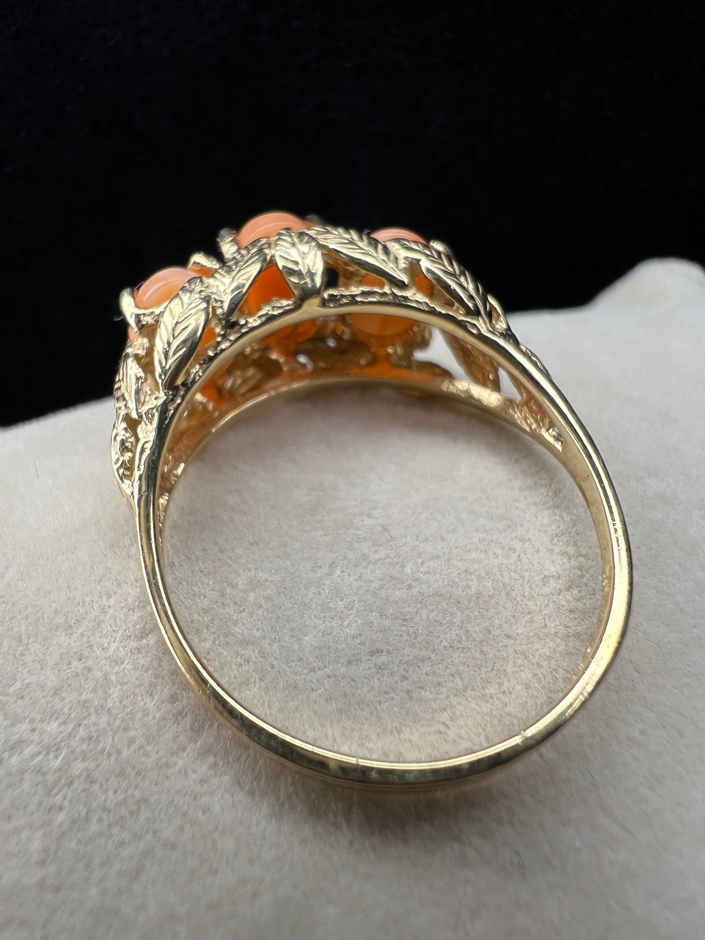This exquisite ring, crafted in the Bahamas from 14 karat gold, features three peachy-salmon coral cabochons elegantly set amid intricately designed gold leaves. The combination of warm coral hues and detailed goldwork creates a distinctive piece.