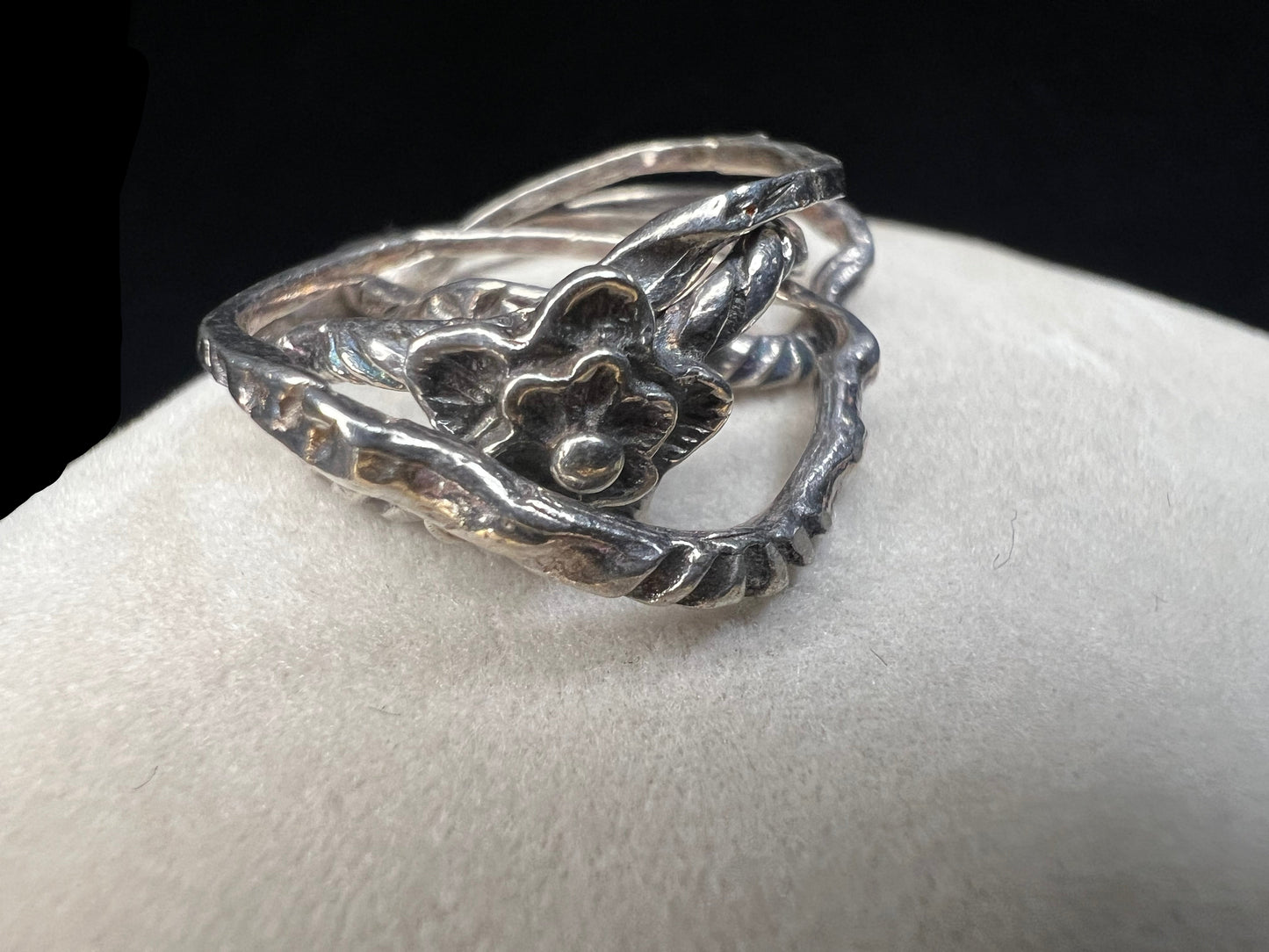This sterling silver flower ring features four interconnected bands, creating a distinctive and elegant twist on a classic design.