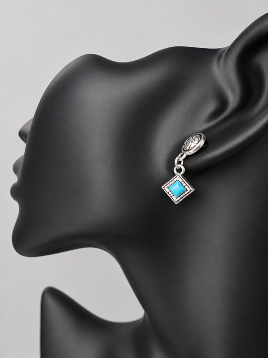 Here are handcrafted sterling silver dangle earrings inspired by native design aesthetics, featuring turquoise accents that swing with natural grace. The intricate silverwork combines traditional artistry with contemporary style, making these earrings a versatile statement piece.