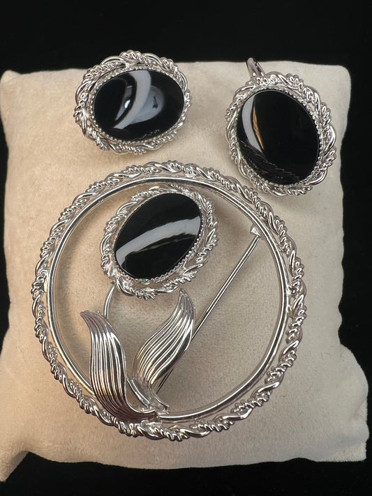 This brooch and earrings set will add sophistication to any outfit. Crafted from fine sterling silver with intricate detail work, the brooch features a flower whose center is an onyx stone. The earrings, which have screw-back closures, are adorned with matching onyx stones.
