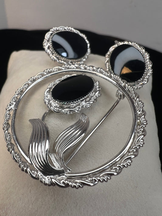 This brooch and earrings set will add sophistication to any outfit. Crafted from fine sterling silver with intricate detail work, the brooch features a flower whose center is an onyx stone. The earrings, which have screw-back closures, are adorned with matching onyx stones.
