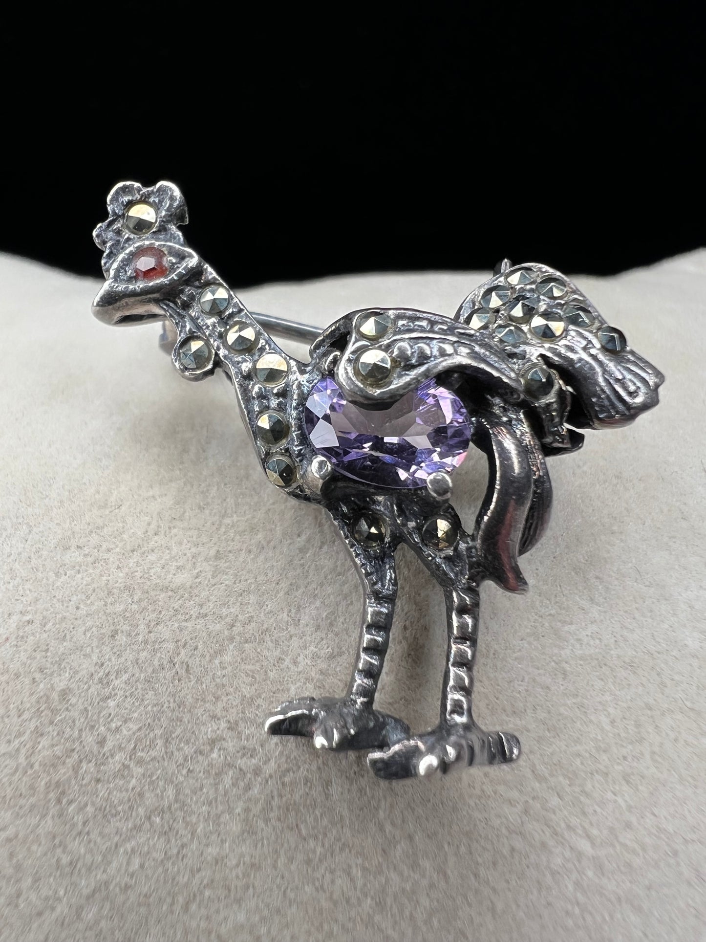 This is a striking mid-century rooster brooch that captures vintage elegance and whimsy. Handcrafted in sterling silver, this statement piece features a vibrant amethyst belly, accented with shimmering marcasite details that catch the light. Perfect for adding character to any outfit or displaying as a collectible treasure.