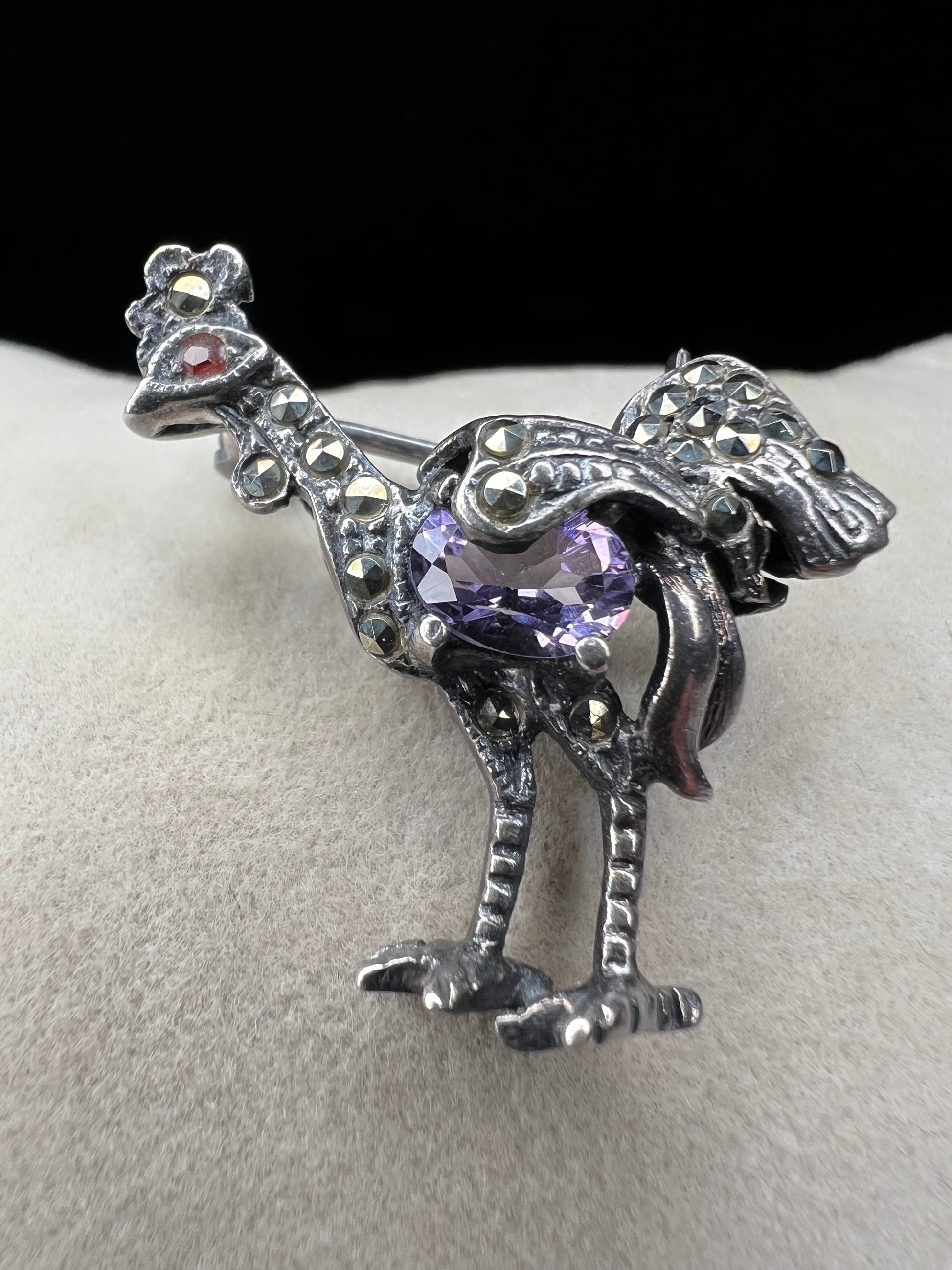 This is a striking mid-century rooster brooch that captures vintage elegance and whimsy. Handcrafted in sterling silver, this statement piece features a vibrant amethyst belly, accented with shimmering marcasite details that catch the light. Perfect for adding character to any outfit or displaying as a collectible treasure.