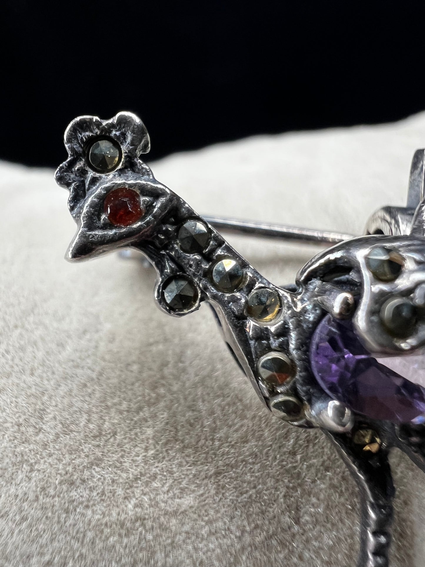 This is a striking mid-century rooster brooch that captures vintage elegance and whimsy. Handcrafted in sterling silver, this statement piece features a vibrant amethyst belly, accented with shimmering marcasite details that catch the light. Perfect for adding character to any outfit or displaying as a collectible treasure.