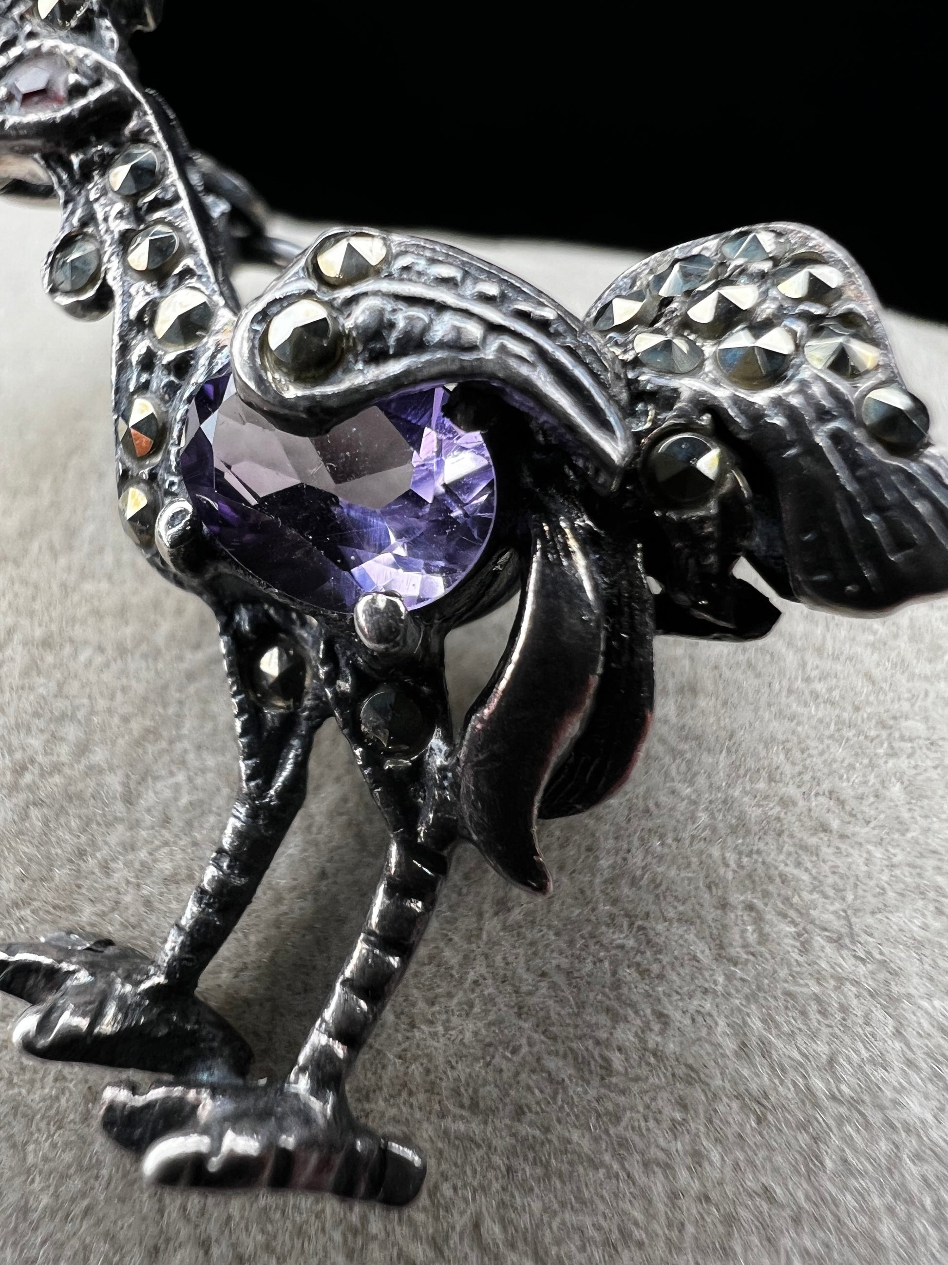 This is a striking mid-century rooster brooch that captures vintage elegance and whimsy. Handcrafted in sterling silver, this statement piece features a vibrant amethyst belly, accented with shimmering marcasite details that catch the light. Perfect for adding character to any outfit or displaying as a collectible treasure.