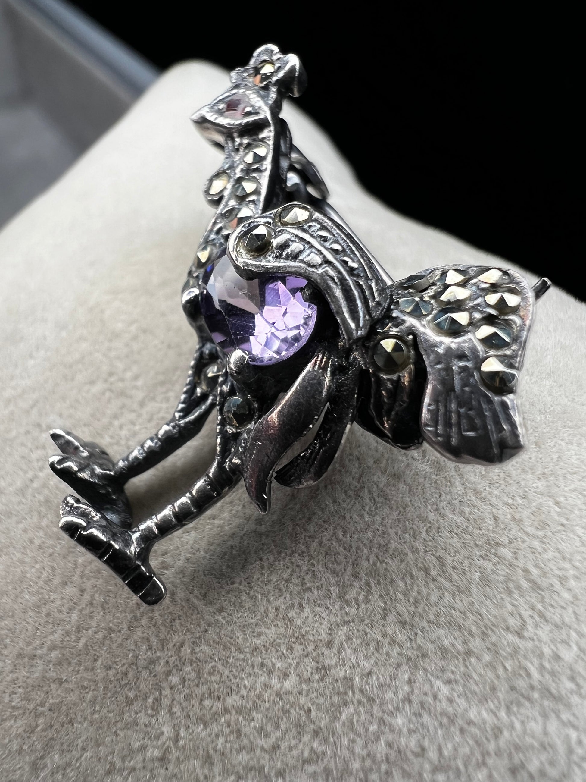 This is a striking mid-century rooster brooch that captures vintage elegance and whimsy. Handcrafted in sterling silver, this statement piece features a vibrant amethyst belly, accented with shimmering marcasite details that catch the light. Perfect for adding character to any outfit or displaying as a collectible treasure.