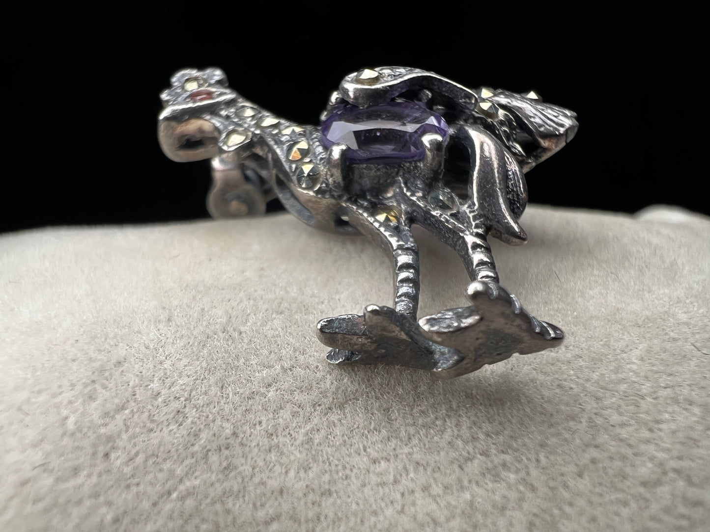 This is a striking mid-century rooster brooch that captures vintage elegance and whimsy. Handcrafted in sterling silver, this statement piece features a vibrant amethyst belly, accented with shimmering marcasite details that catch the light. Perfect for adding character to any outfit or displaying as a collectible treasure.