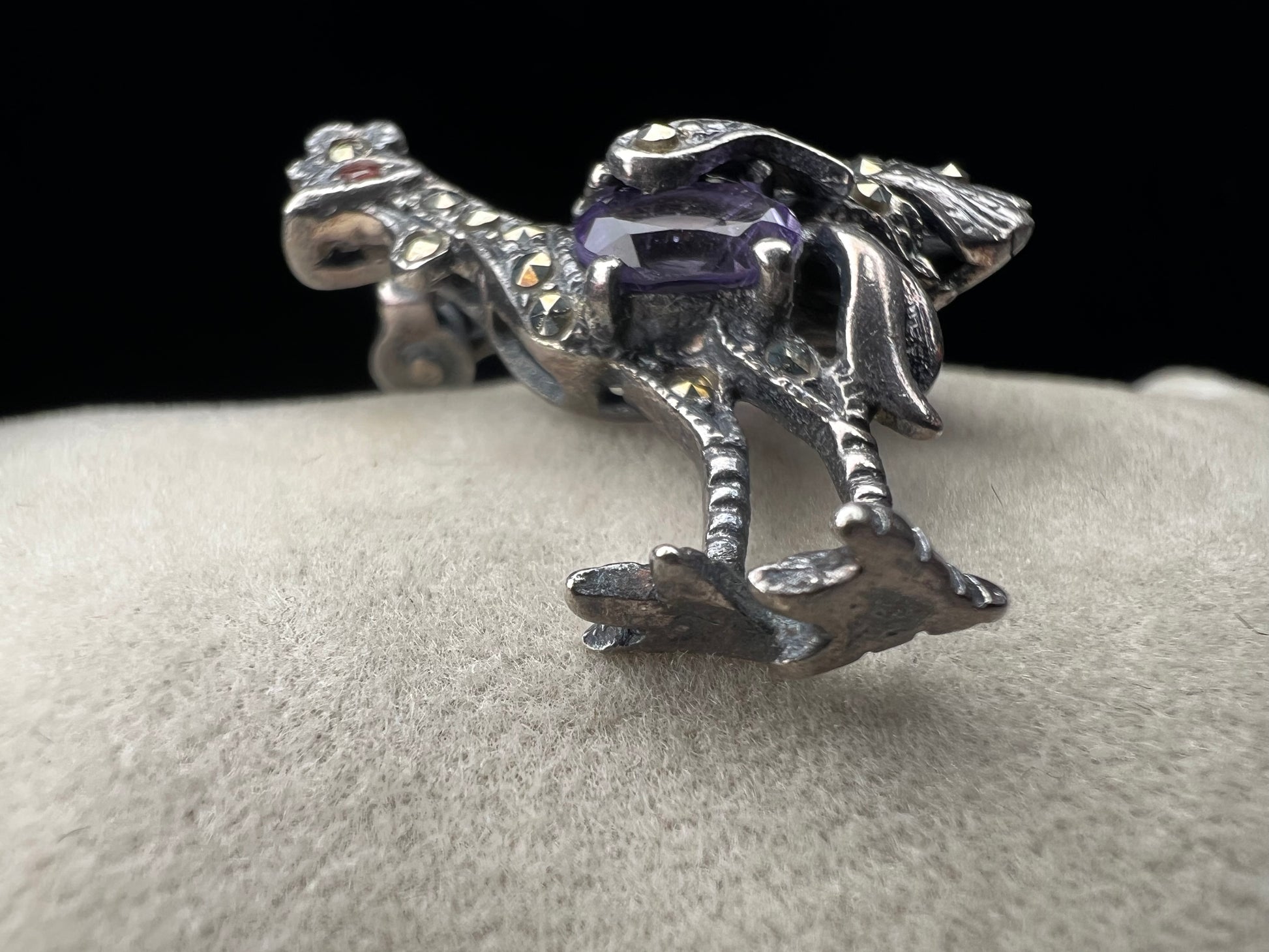 This is a striking mid-century rooster brooch that captures vintage elegance and whimsy. Handcrafted in sterling silver, this statement piece features a vibrant amethyst belly, accented with shimmering marcasite details that catch the light. Perfect for adding character to any outfit or displaying as a collectible treasure.