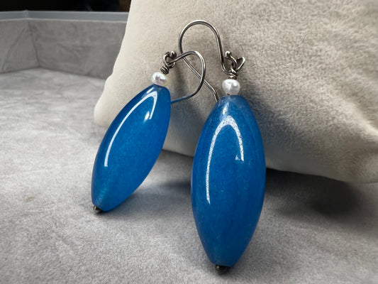 These earrings feature natural blue stones that captivate with their vibrant hue, elegantly complemented by delicate pearls. Crafted with sterling silver components, they combine quality materials and distinctive design.