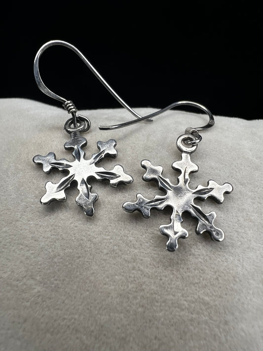 These sterling silver earrings feature intricate texture on both sides of each snowflake, designed to catch and reflect light with every movement. Ideal for complementing winter outfits, they offer a subtle yet elegant touch of seasonal charm.