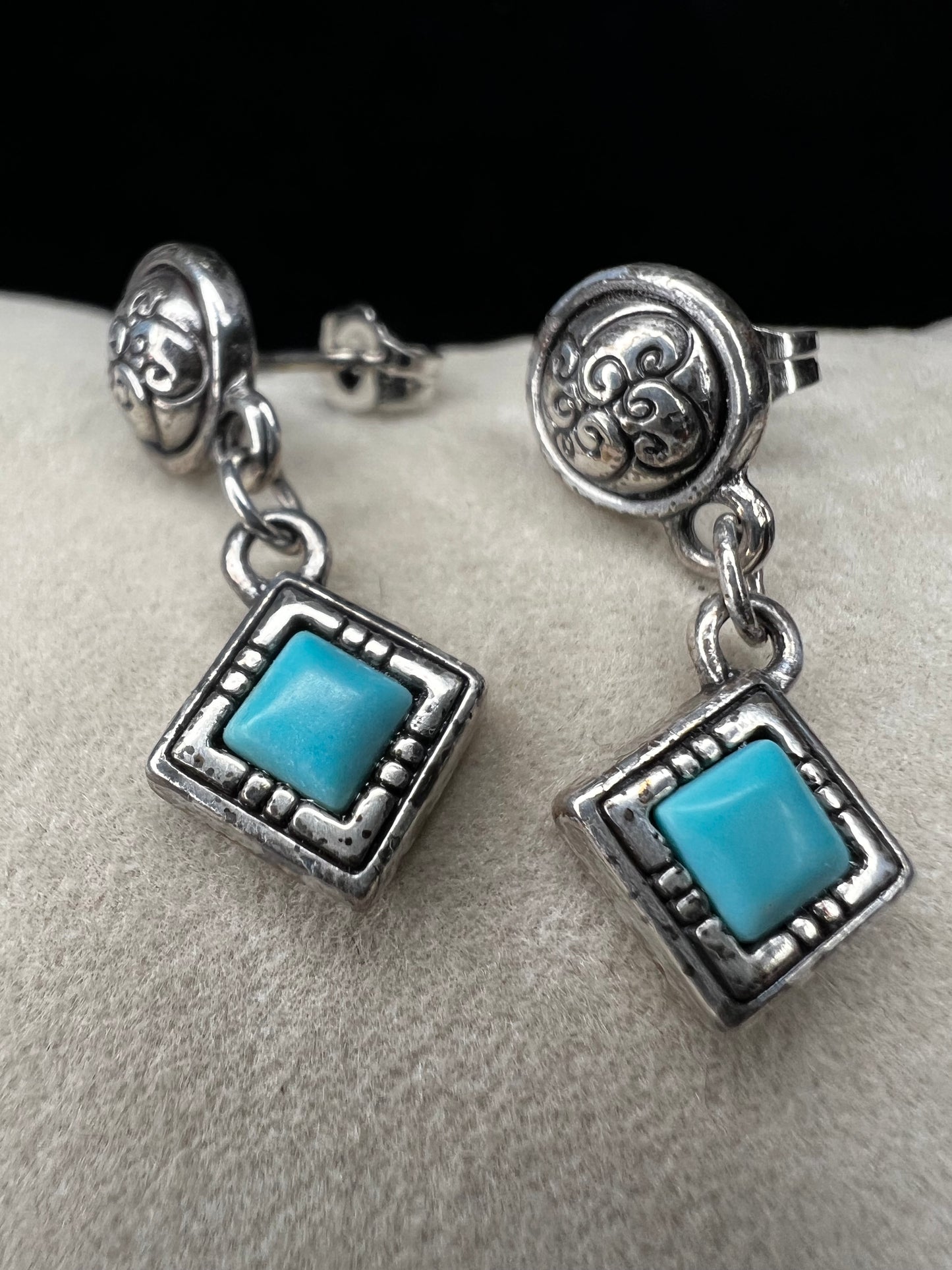 Here are handcrafted sterling silver dangle earrings inspired by native design aesthetics, featuring turquoise accents that swing with natural grace. The intricate silverwork combines traditional artistry with contemporary style, making these earrings a versatile statement piece.