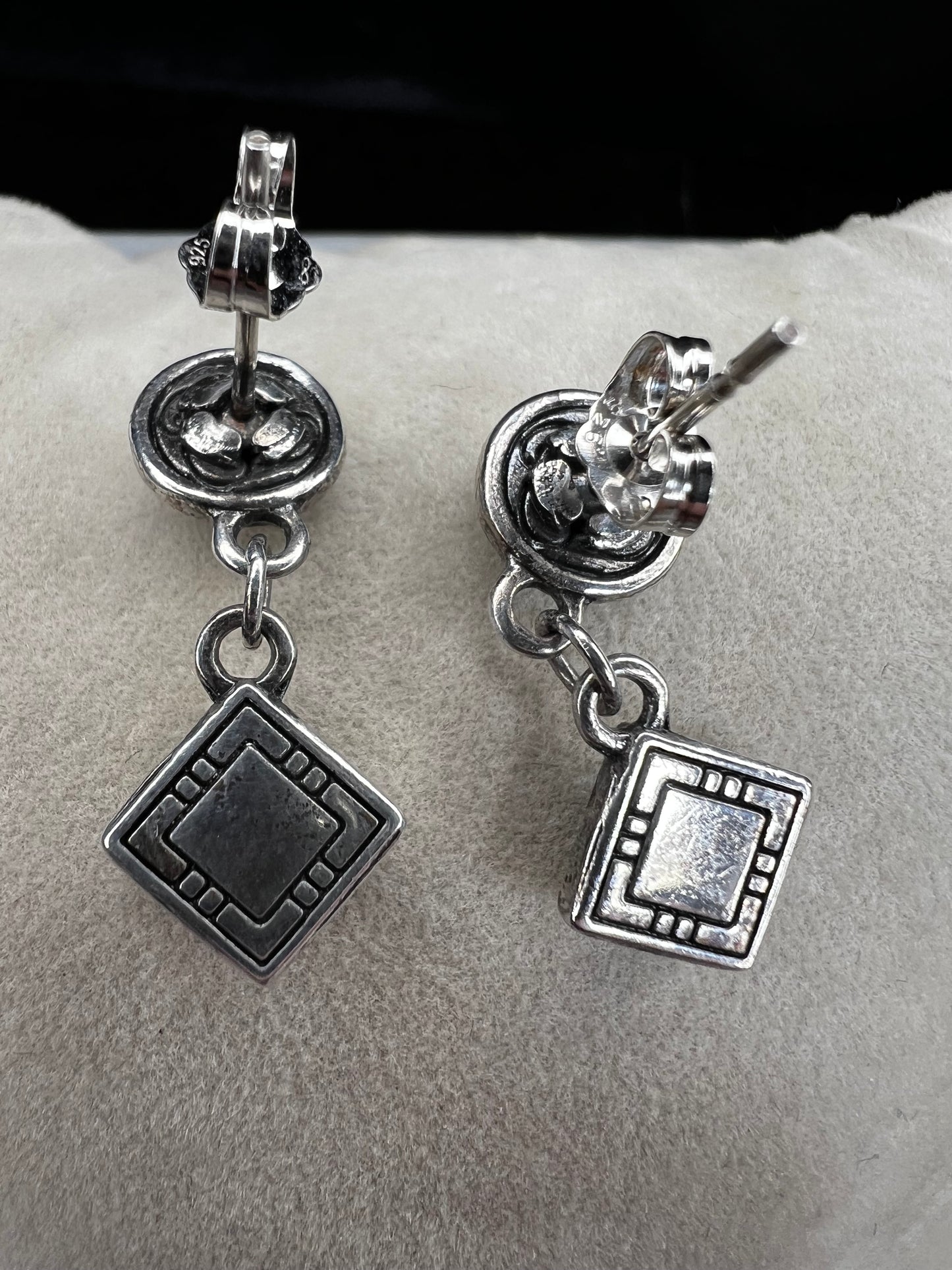 Here are handcrafted sterling silver dangle earrings inspired by native design aesthetics, featuring turquoise accents that swing with natural grace. The intricate silverwork combines traditional artistry with contemporary style, making these earrings a versatile statement piece.