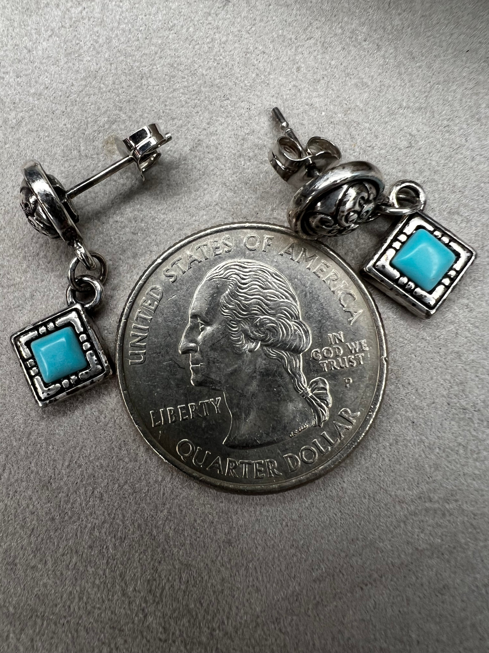 Here are handcrafted sterling silver dangle earrings inspired by native design aesthetics, featuring turquoise accents that swing with natural grace. The intricate silverwork combines traditional artistry with contemporary style, making these earrings a versatile statement piece.