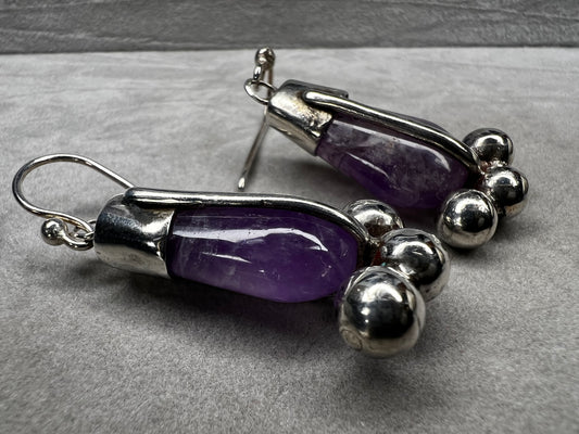 These vintage sterling silver drop earrings feature striking amethyst stones. Their distinctive design combines classic elegance with a bold, unique style, making them an exceptional accessory.