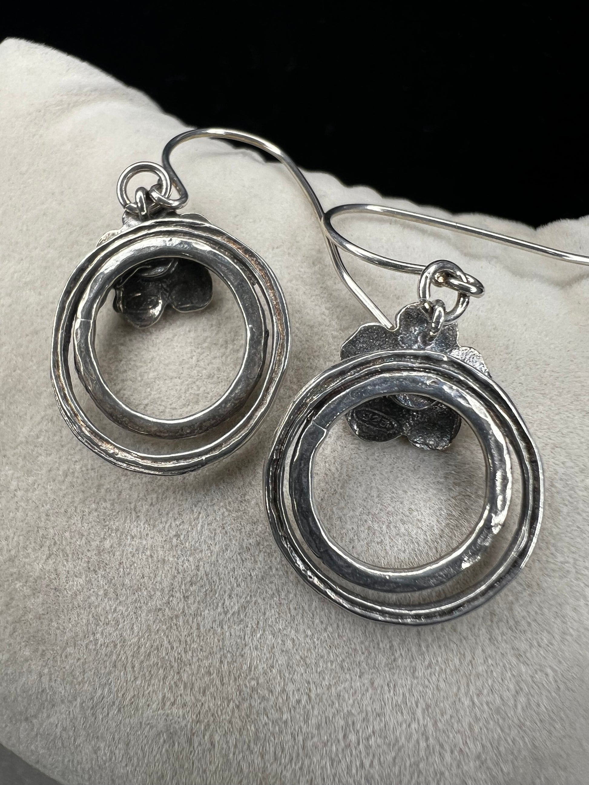 These sterling silver earrings showcase a flower design with a lustrous pearl at its center, elegantly positioned atop a double hoop. The combination offers a refined aesthetic, perfect for adding a sophisticated touch to any ensemble.