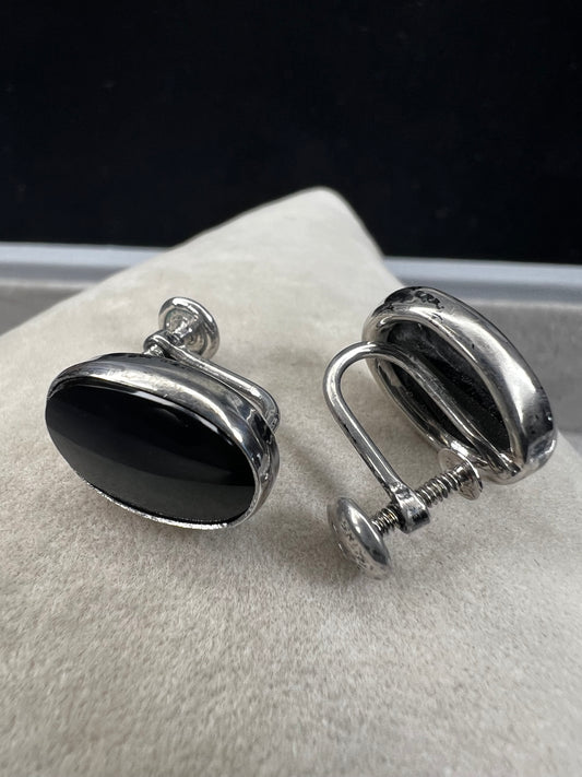 These vintage sterling silver screw-back earrings showcase an elegant oval jet stone, offering a timeless and sophisticated accessory. The secure screw-back design ensures comfortable wear without piercing, making them ideal for collectors and those seeking classic style with reliable functionality.