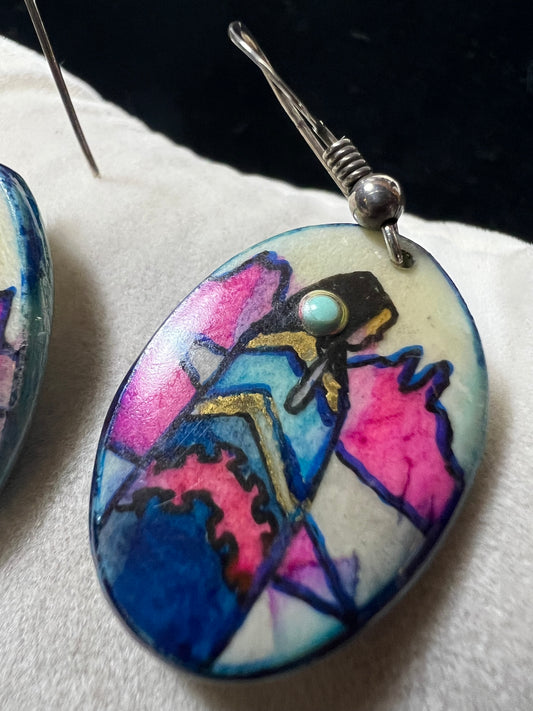 These vintage handmade earrings showcase a vibrant native scene on a lightweight material, expertly crafted to highlight intricate details and rich colors. They are completed with sterling silver hooks.