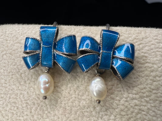 Pair of blue bow-shaped earrings with pearl drops on a textured surface.