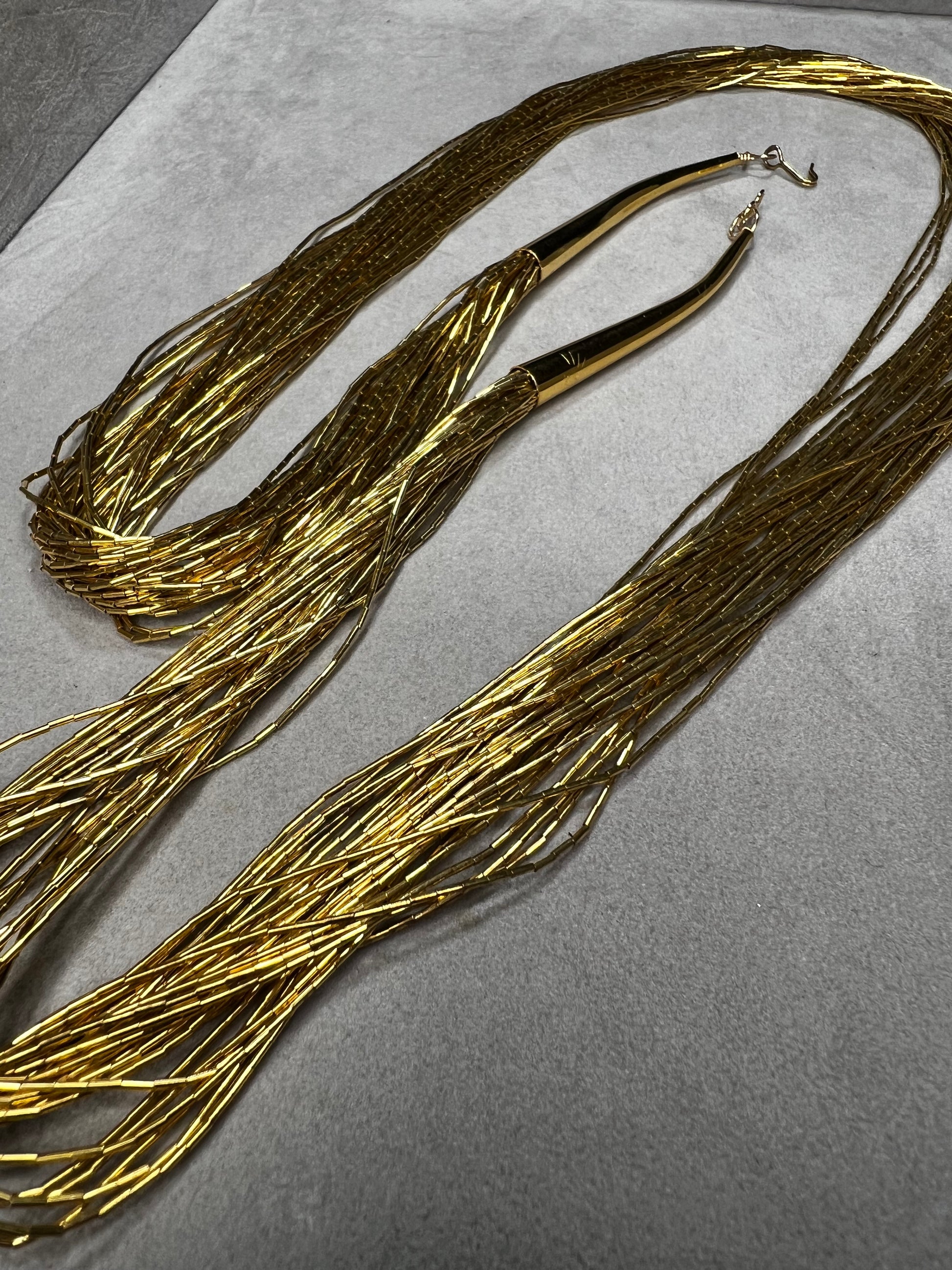 This is a striking gold over sterling silver necklace, featuring the iconic liquid-sterling design. The fluid, sculptural form creates visual movement and dimension, while the gold overlay adds warmth and luxury to the cool brilliance of sterling silver. With substantial length and thickness, this piece commands attention as a standalone statement.