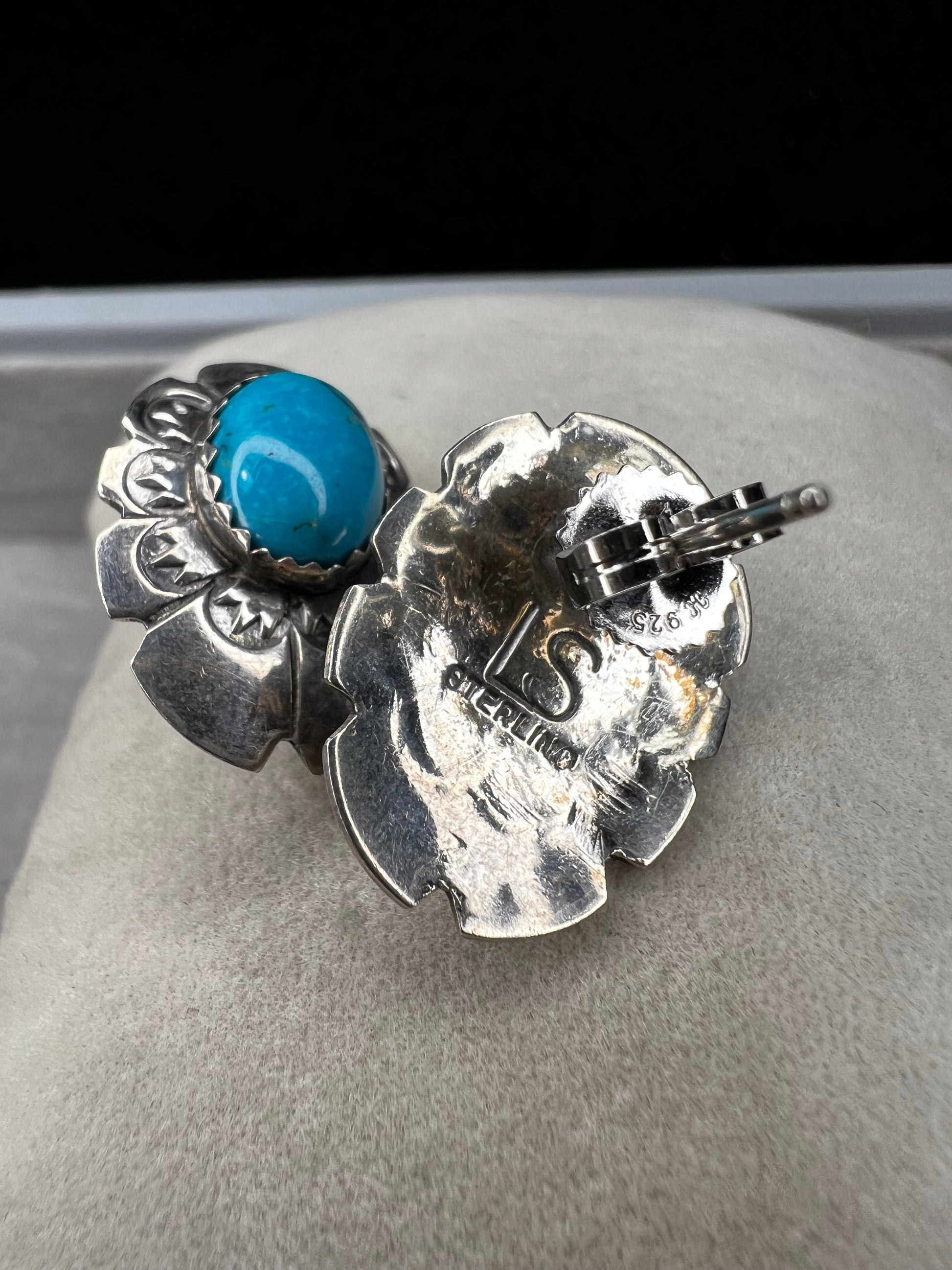 These sterling silver earrings showcase expertly crafted faux turquoise stones, set within intricately detailed silver settings. Signed LS.