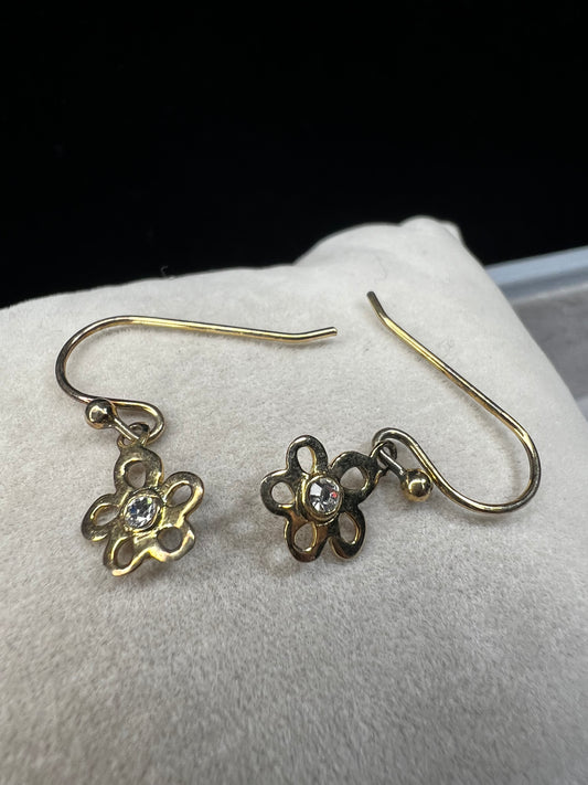 Crafted from sterling silver with a gold overlay, these earrings feature a small flower that hangs just below the ear.