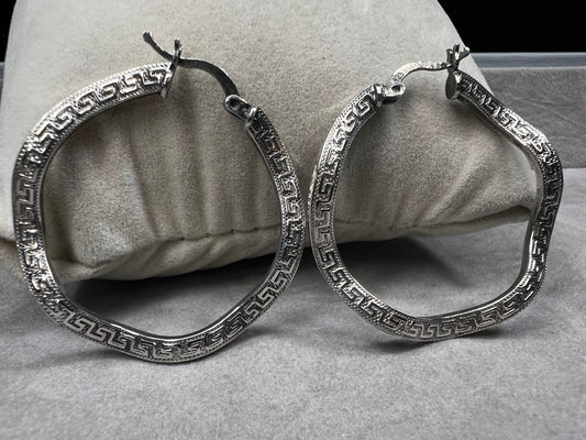 These sterling silver hoop earrings showcase a wavy design enhanced by a timeless Greek key pattern. They combine classic motifs with modern elegance, making them a versatile accessory.