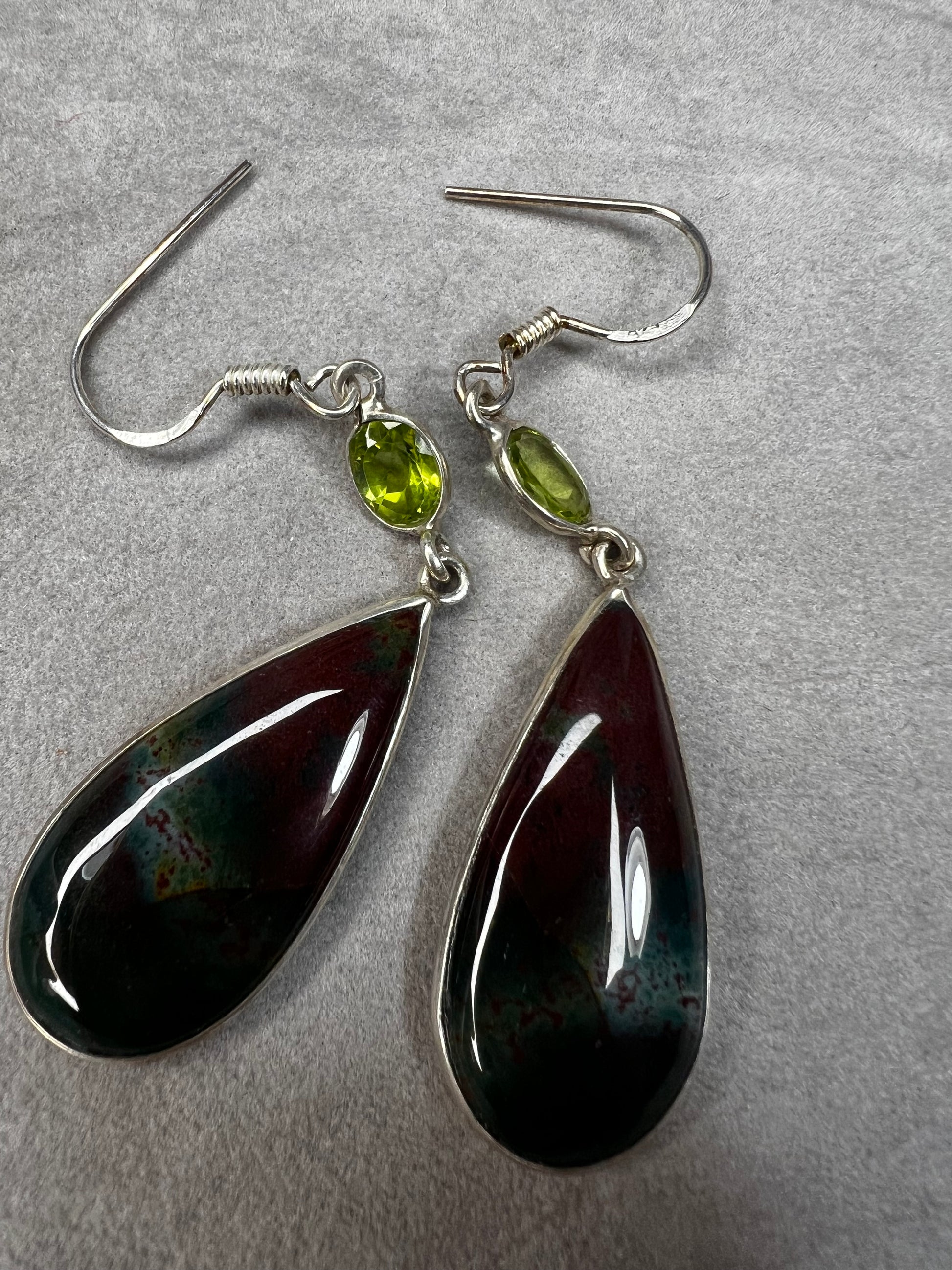 These sterling silver earrings feature a large teardrop-shaped bloodstone paired with a bright peridot, creating a distinctive and elegant look.