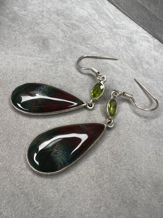 These sterling silver earrings feature a large teardrop-shaped bloodstone paired with a bright peridot, creating a distinctive and elegant look.