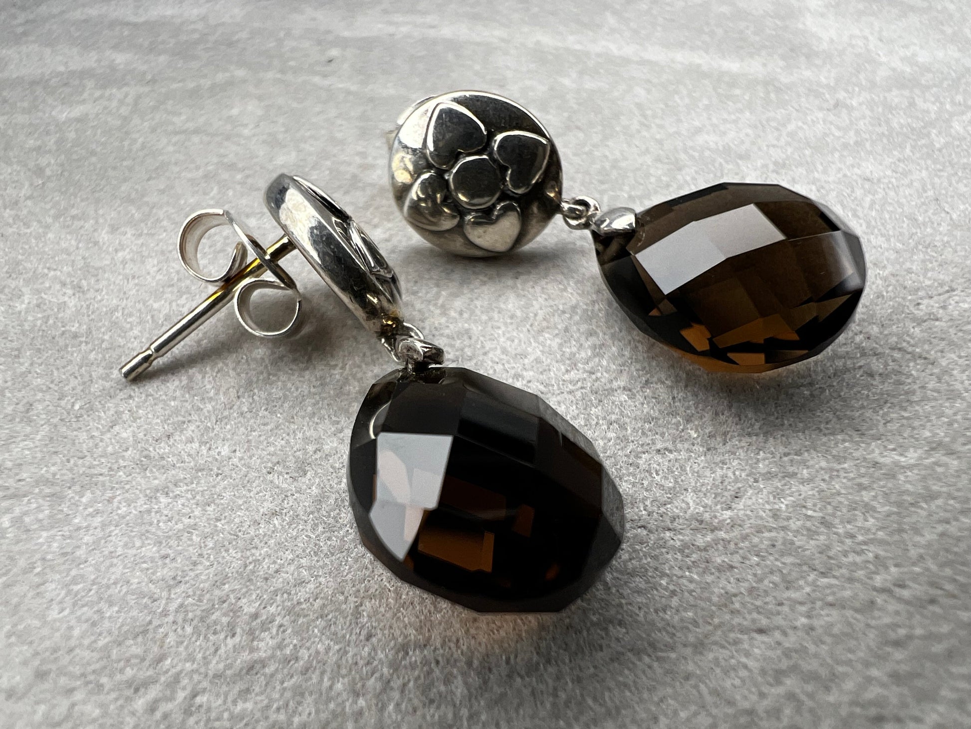 These sterling silver drop earrings feature a delicate flower design button paired with a faceted smoky quartz pendant. Their elegant combination will add a touch of natural beauty and subtle sophistication to your outfit.