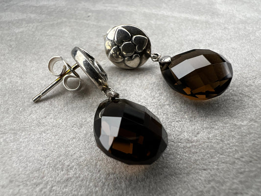 These sterling silver drop earrings feature a delicate flower design button paired with a faceted smoky quartz pendant. Their elegant combination will add a touch of natural beauty and subtle sophistication to your outfit.