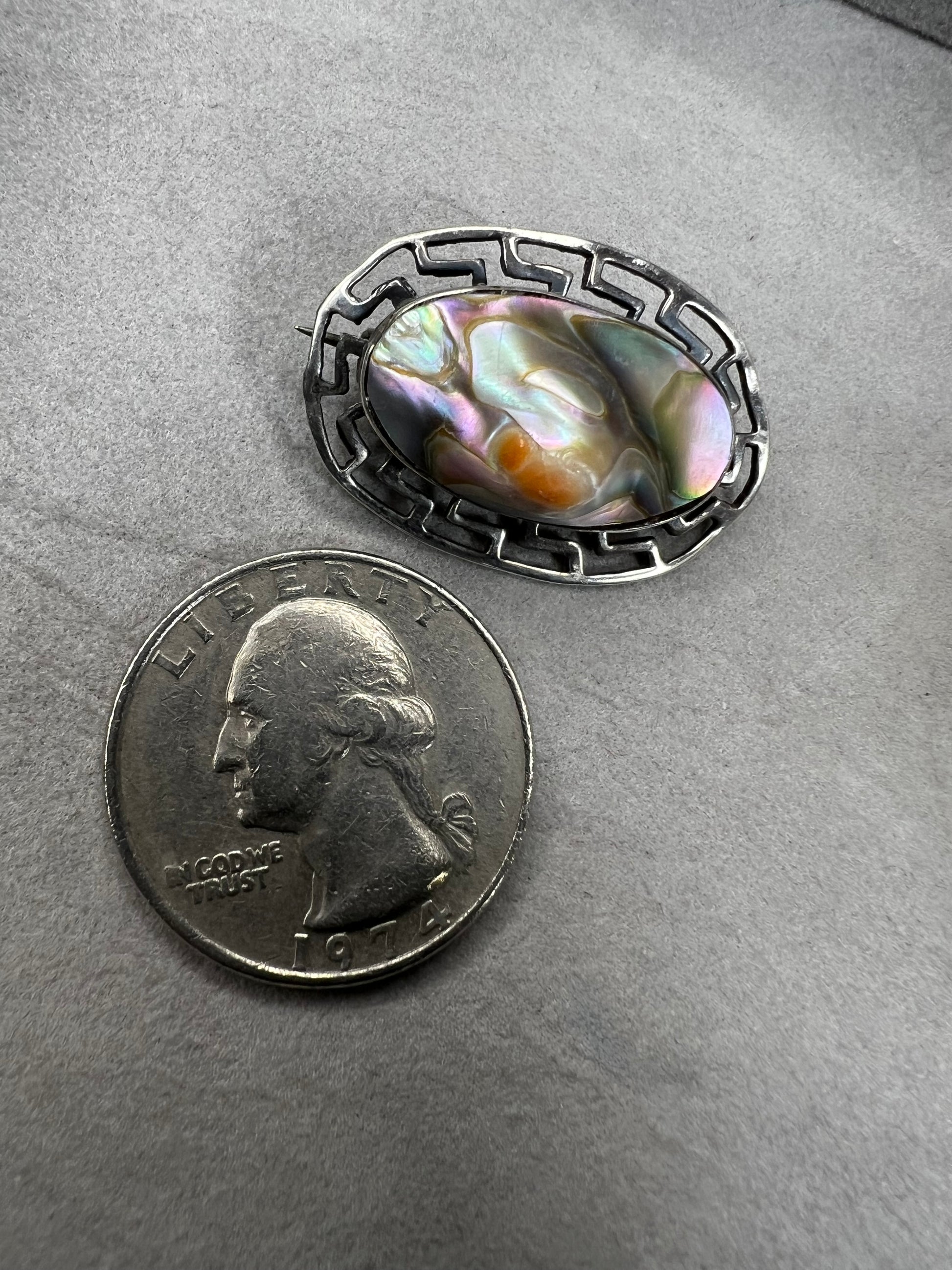 This vintage brooch showcases a tall abalone shell beautifully set within a sterling silver frame that features a classic Greek key design. Its elegant combination of natural iridescence and timeless pattern makes it a standout accessory that adds refined charm to any ensemble.