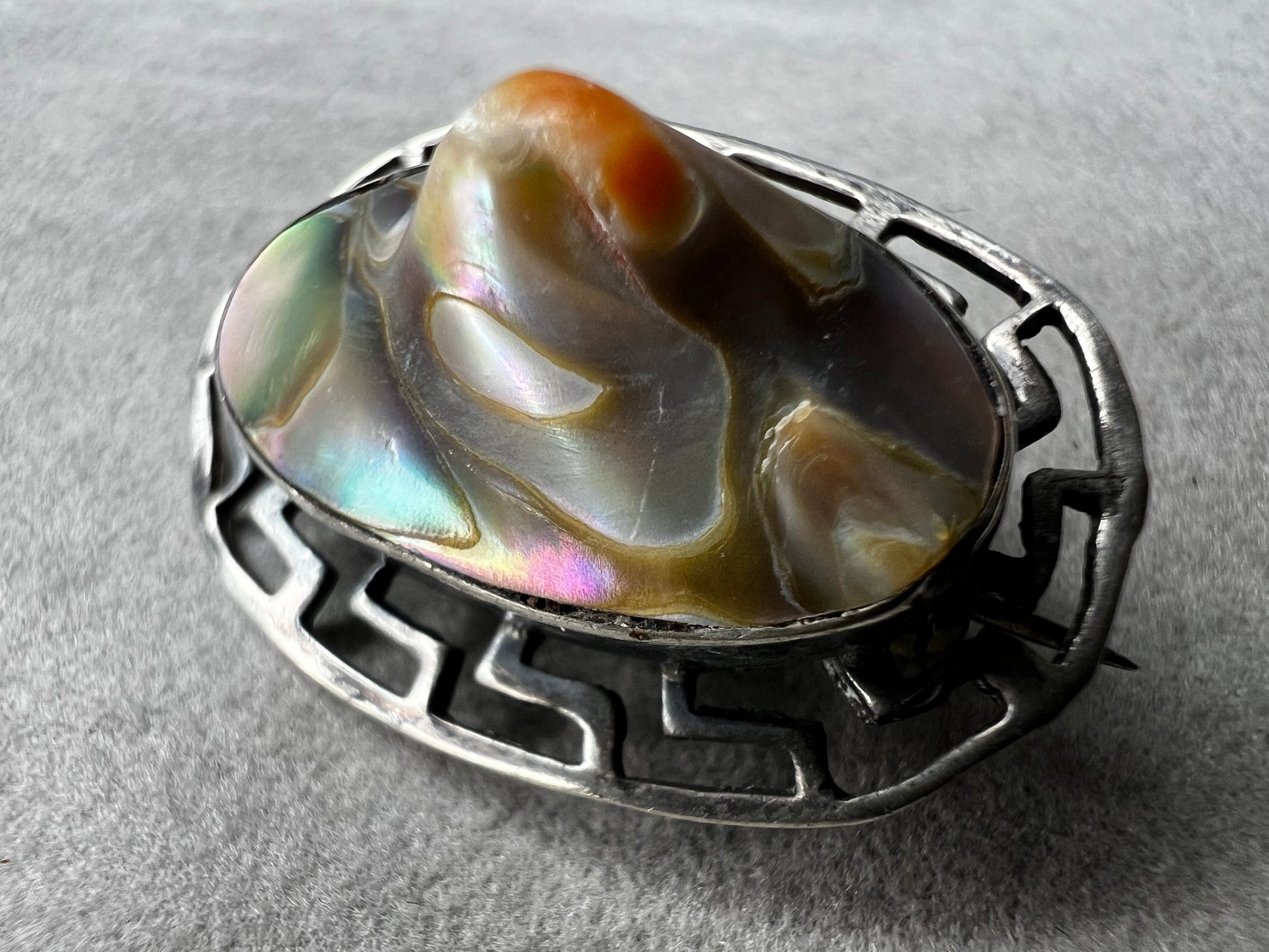 This vintage brooch showcases a tall abalone shell beautifully set within a sterling silver frame that features a classic Greek key design. Its elegant combination of natural iridescence and timeless pattern makes it a standout accessory that adds refined charm to any ensemble.
